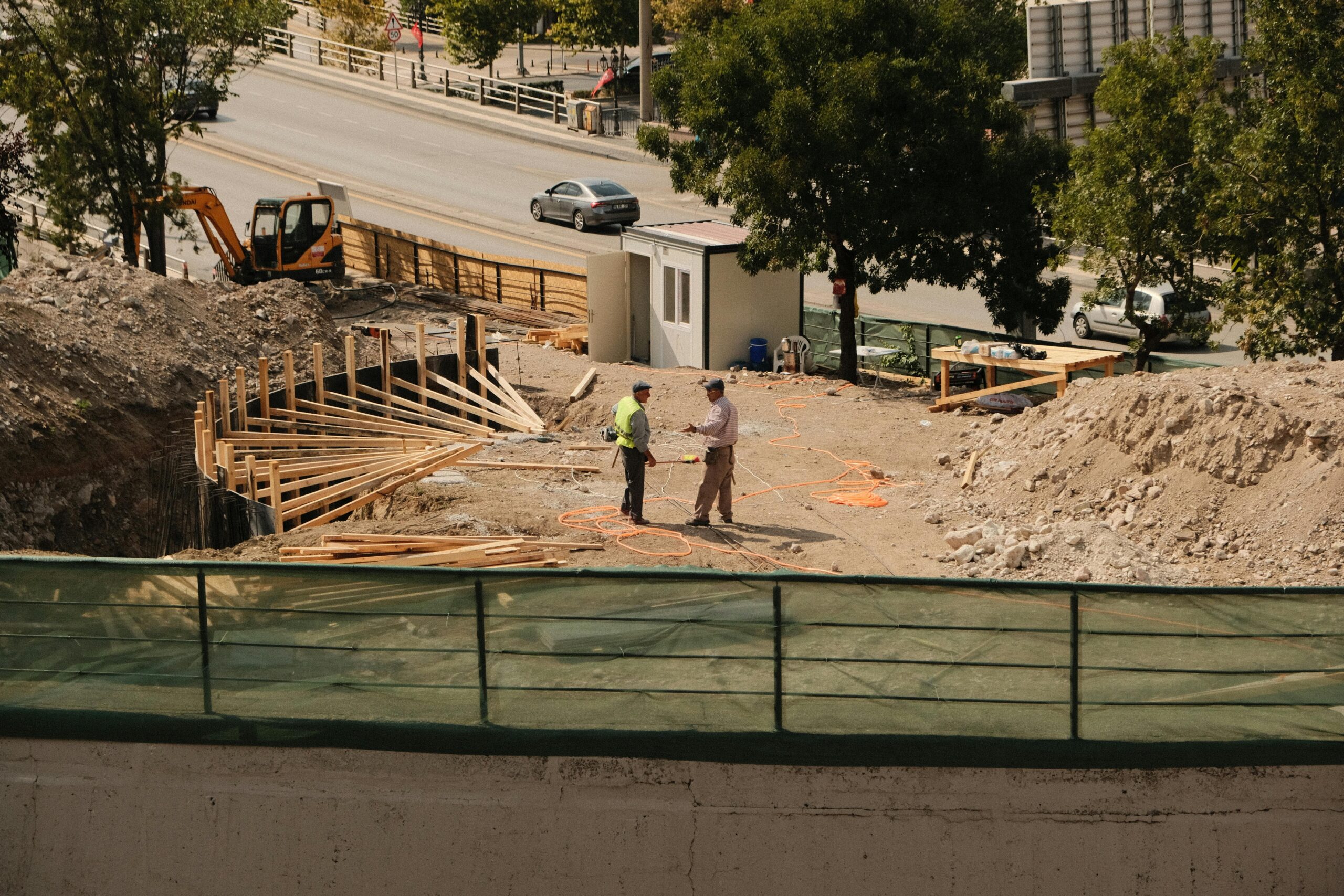 Two engineers discussing plans at an active construction site under sunny skies.